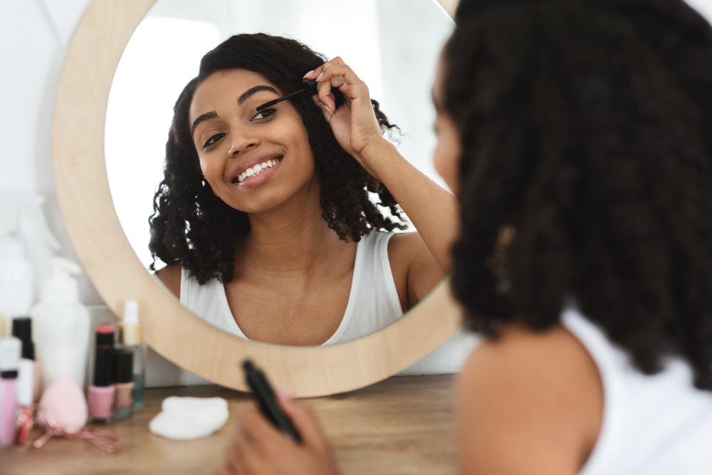 Woman applying mascara to her eye lashes while looking in the mirror