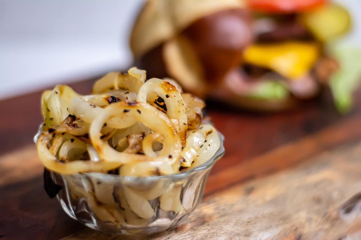 grilled onions in a glass bowl on a cutting board.