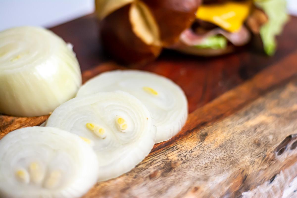 yellow onions sliced in front of a hamburger.