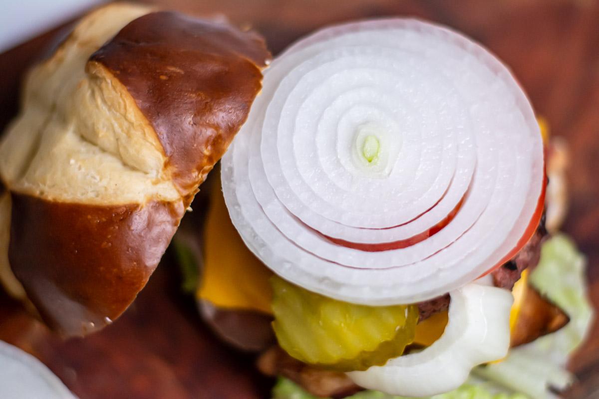 white onion sliced thin on top of a burger with cheese, lettuce, cheese and bacon.