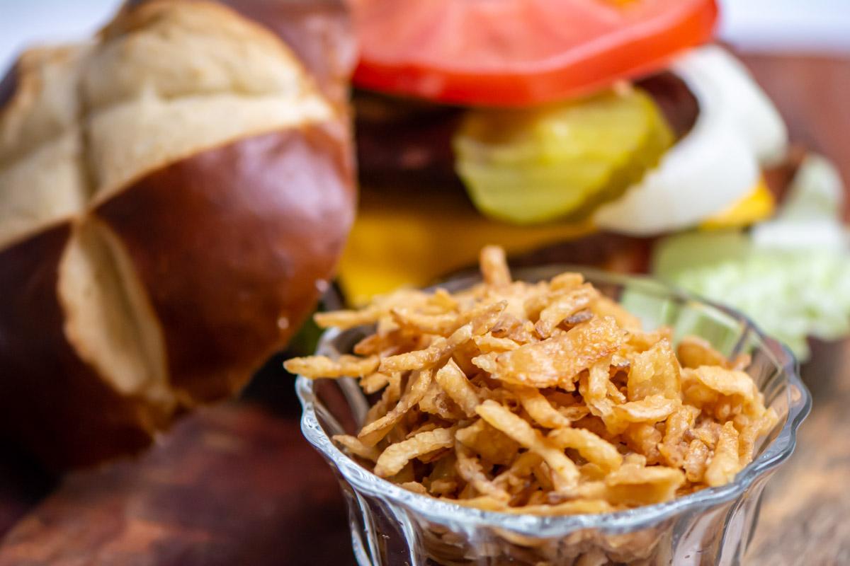 crispy fried onions in a glass container in front of a hamburger.