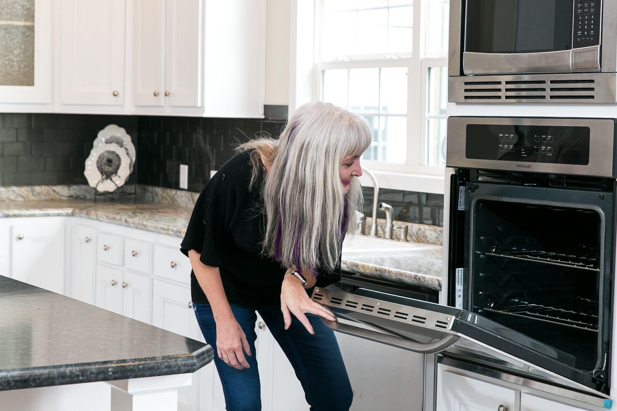 A woman touring a Clayton home bends down to look into the stainless steel oven in a kitchen.
