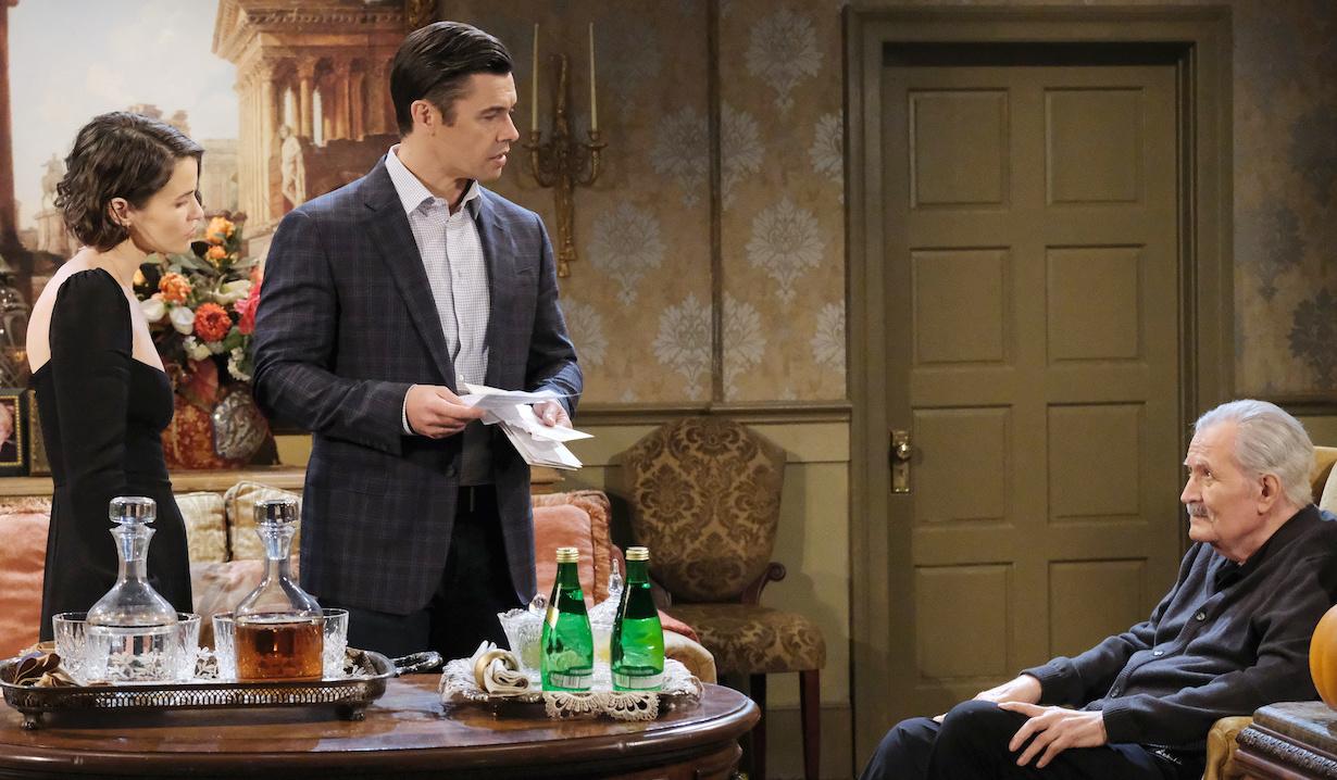 Standing with Sarah, Xander holds bills, and glares at a sitting Victor at the Kiriakis mansion