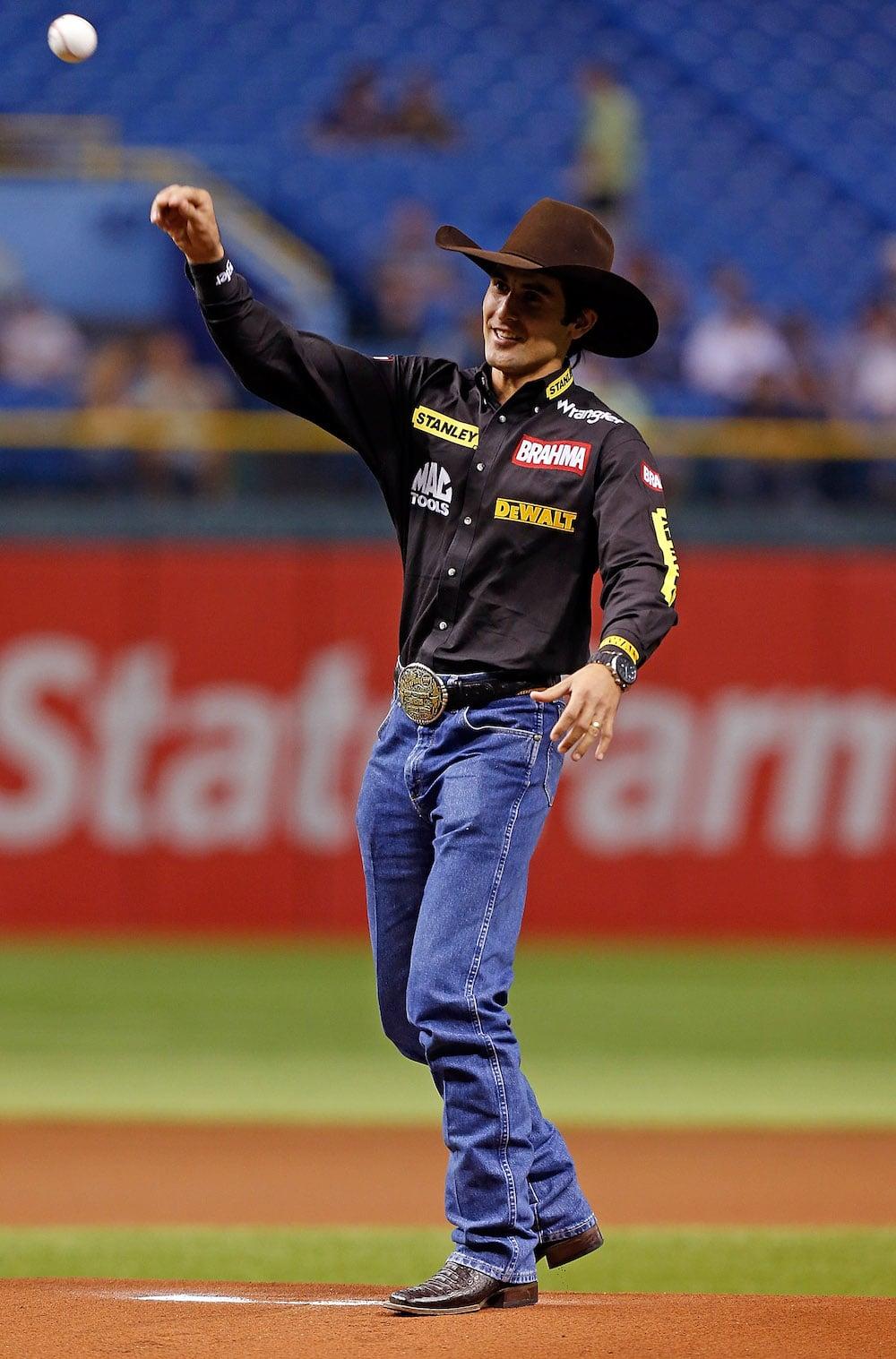 Silvano Alves throws out the ceremonial first pitch in the 2012 Red Sox and Rays game. He is wearing a black cherry felt cowboy hat and his sponsorship shirt.