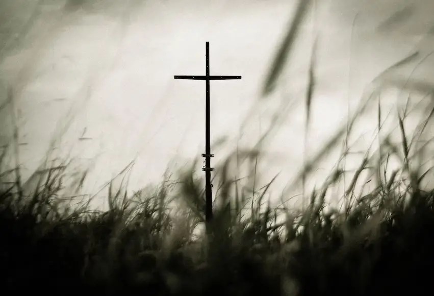 A single cross stands tall in a peaceful field of grass
