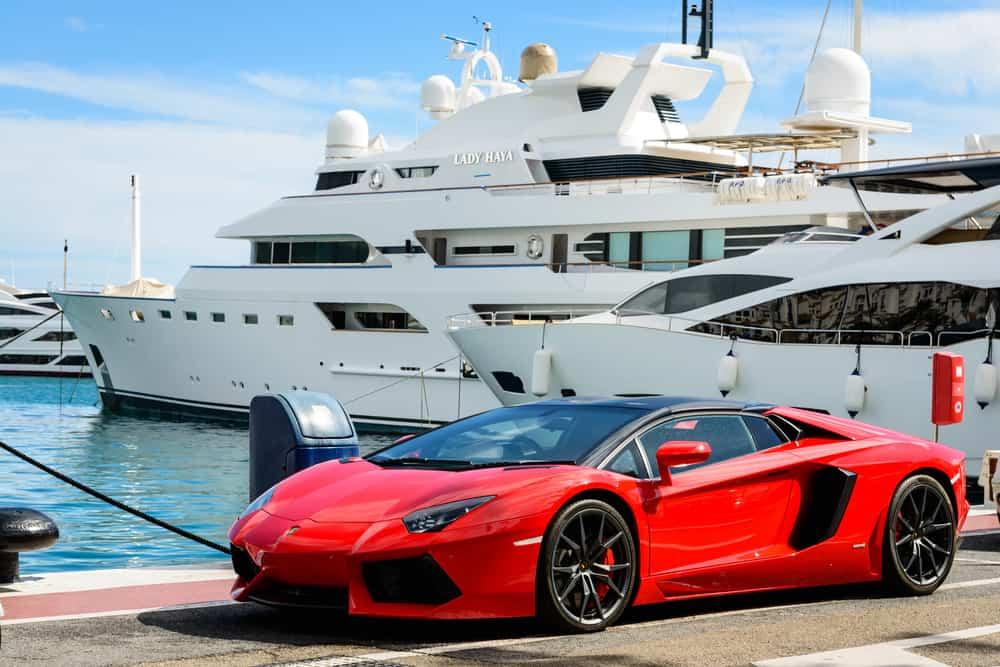 Front view of a red super sport car (Lamborghini) parked alongside luxury yachts moored in the marina of Puerto Jose Banus, Spain