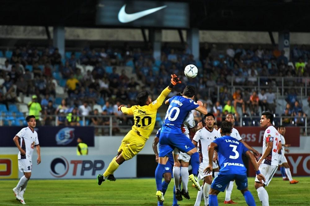 A close look at an ongoing soccer game with the goalie reaching for the ball above the opponent.