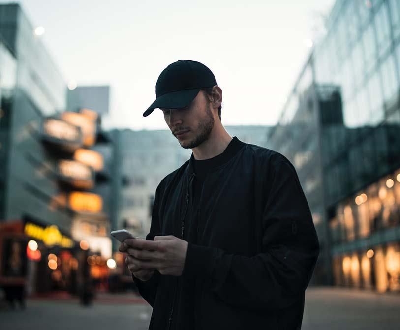 A man in a black jacket wearing a black fitted cap while using the phone