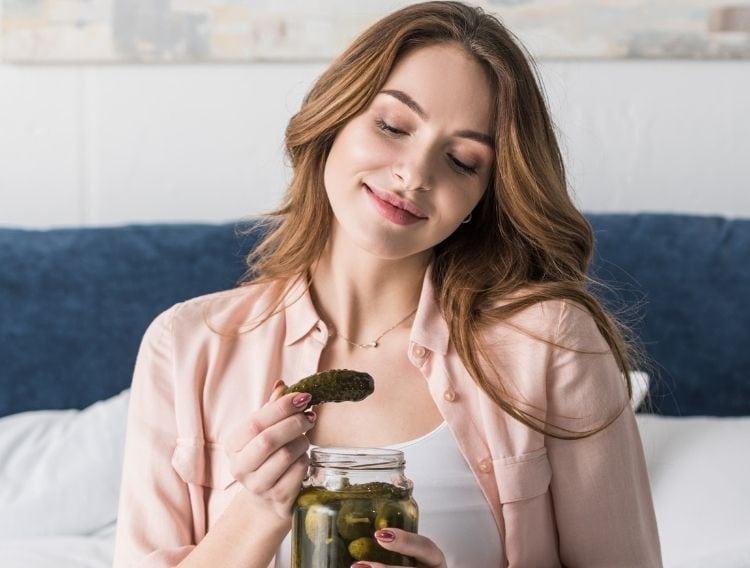 woman-sitting-on-bed-smiling-while-staring-at-a-pickle-from-a-jar.