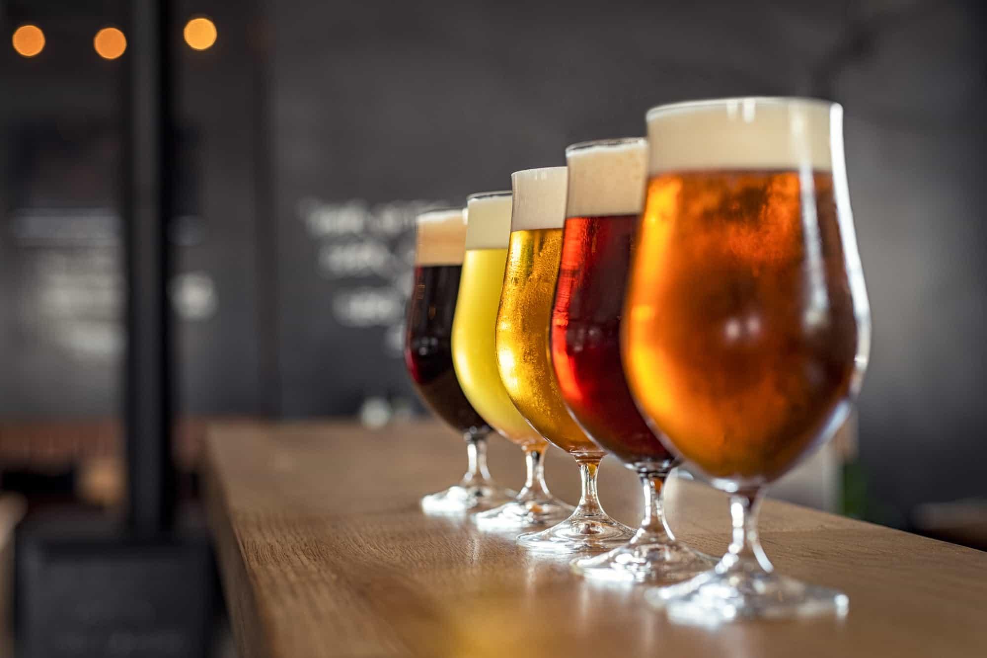 5 glasses of beer sit in a row with varying degrees of darkness