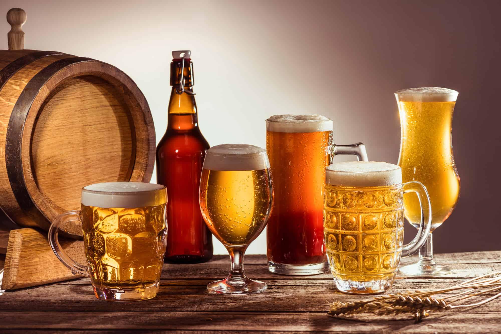 a variety of beer glasses and bottles sit on a wooden table, if you say "i hate beer," trying different types is a good way to see if you find one you enjoy