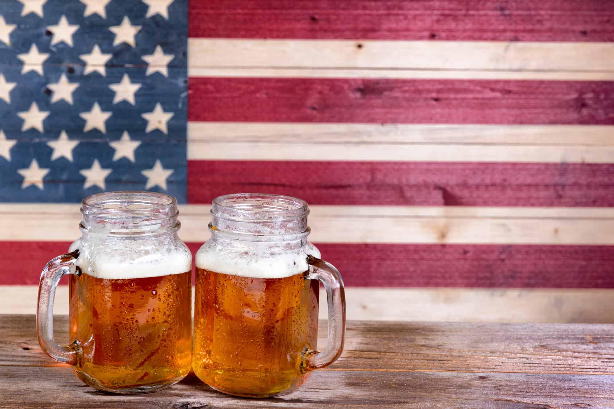 2 beers sit on a wooden table with a wooden american flag as the backdrop