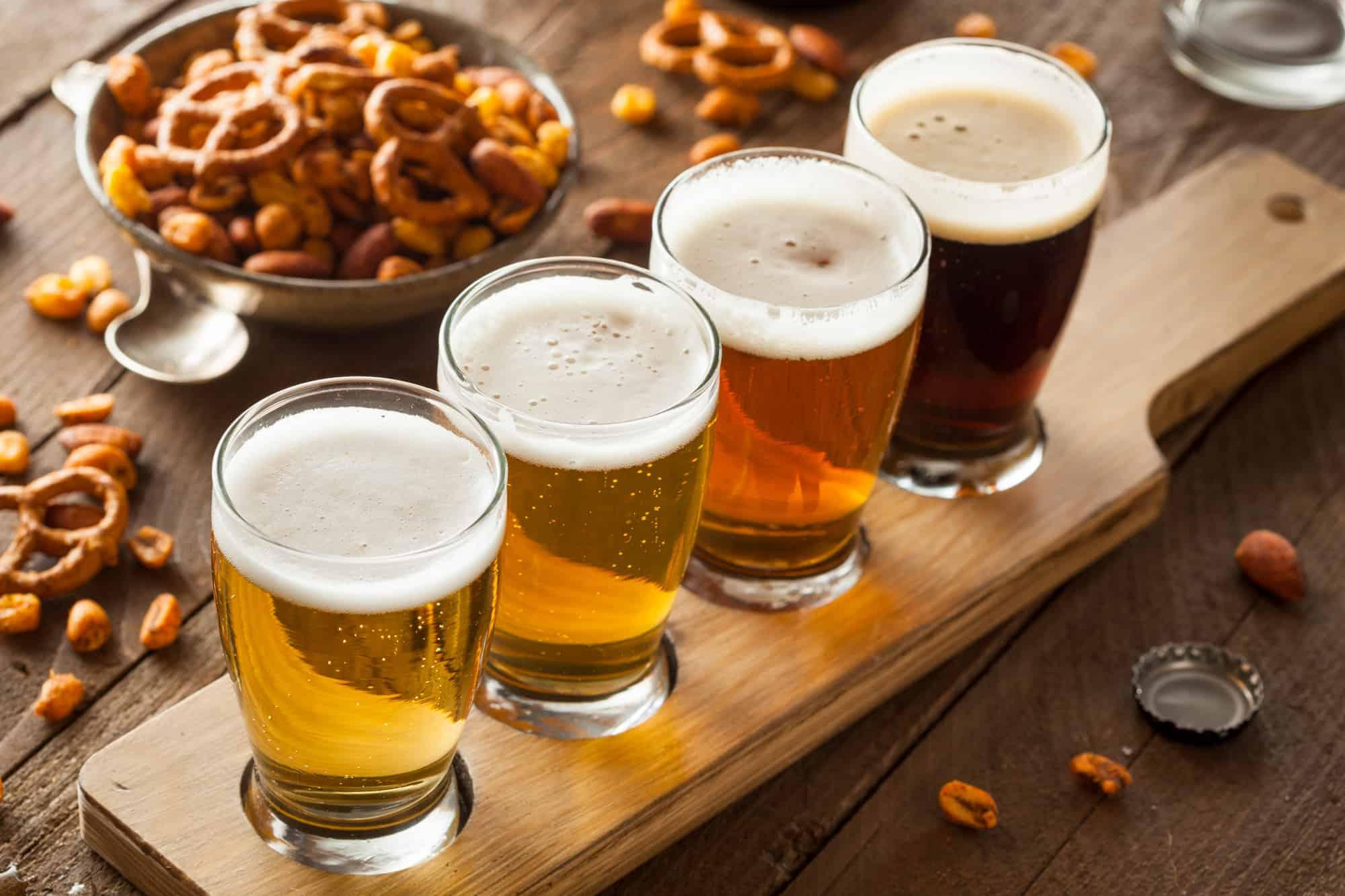 a flight of four beers sits on a table with snack food like pretzels, if you say "i hate beer" then flights are a good option as you can try several beers without having to order a full pint