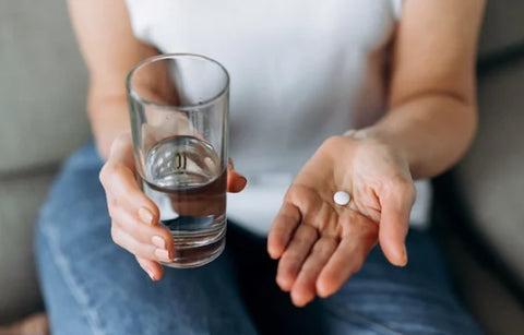 a woman taking a pill with a glass of water