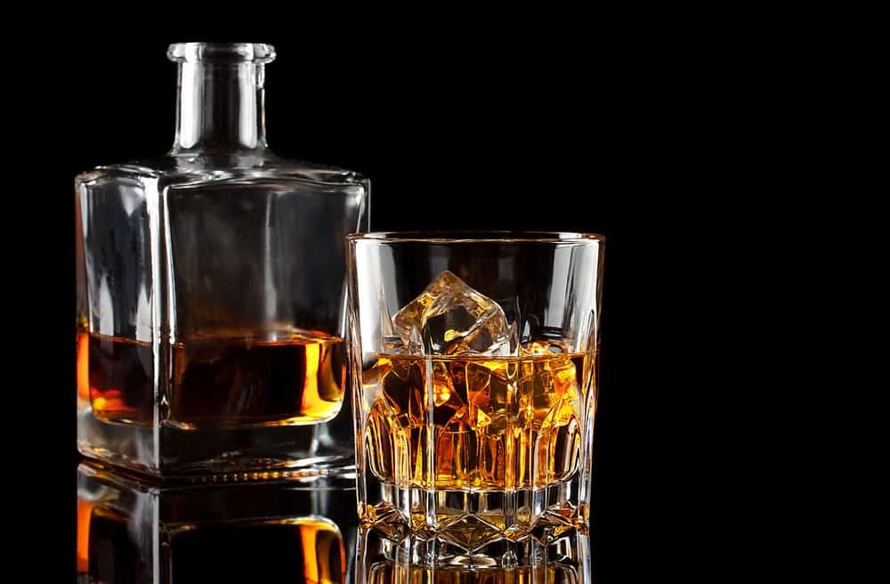 Glass of the whiskey with ice and a square decanter isolated on a black background
