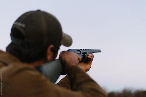 A man looking through the eyehole of his gun and pointing at the sky