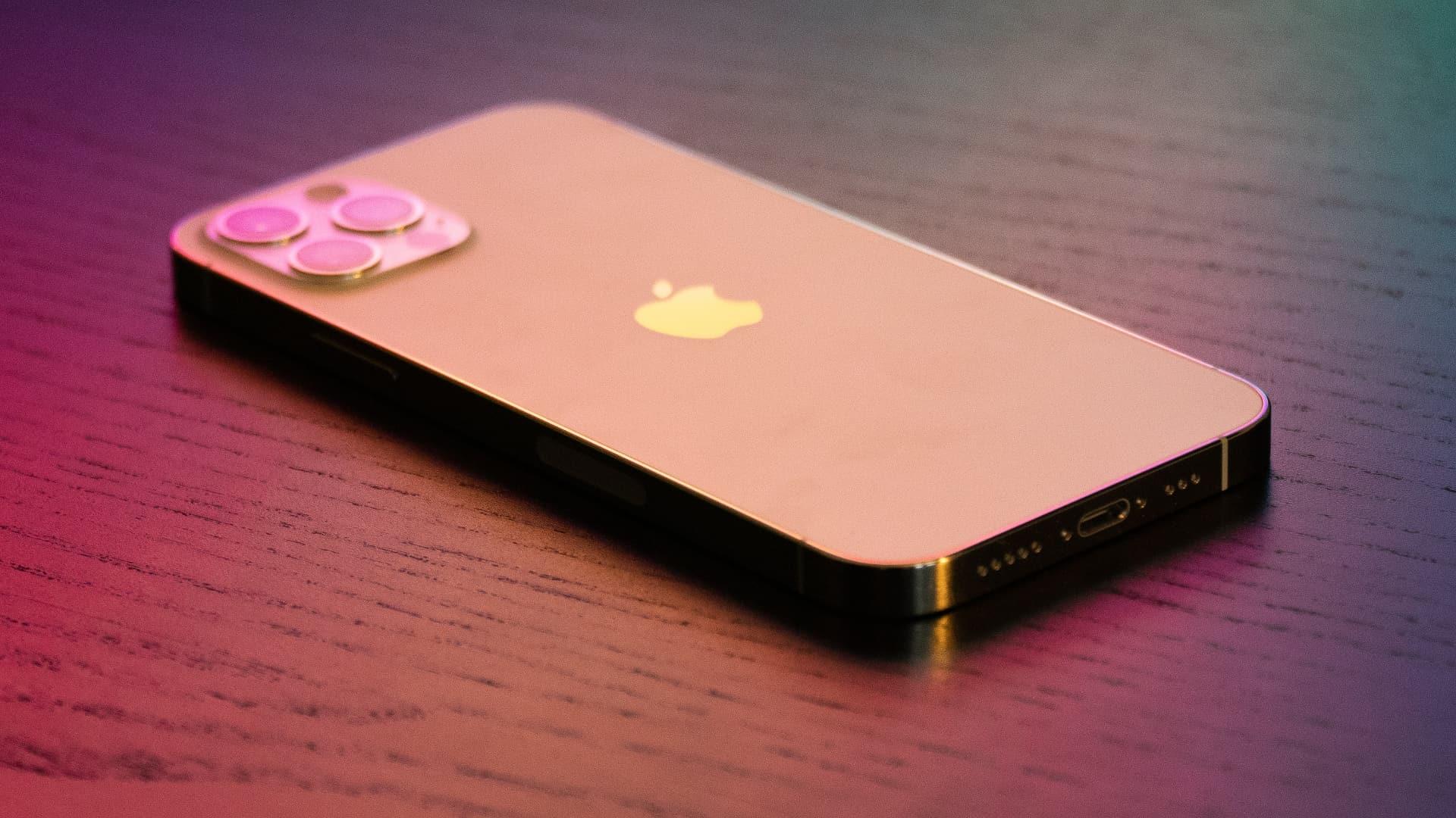 Gold iPhone 12 Pro under colorful lighting, set facedown on a wooden table