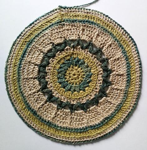 An intricate circle, made out of different shades of green DK weight herbal dyed yarn.