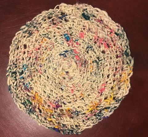 A circle made of white yarn with speckles of multicolored dotted through the white.