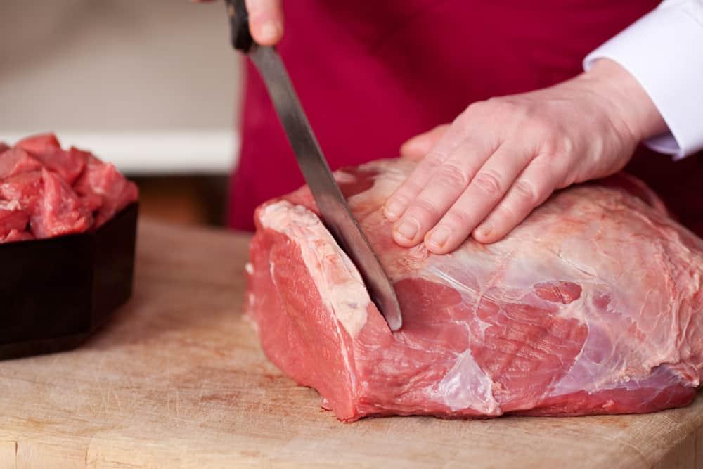 Closeup of the hands of a butcher cutting slices of raw meat