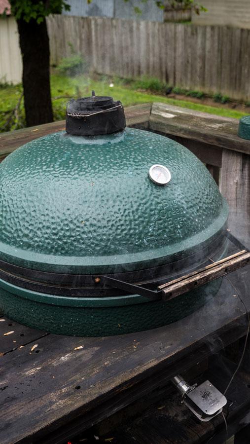 Chimney of a Big Green Egg wafting thin blue smoke.