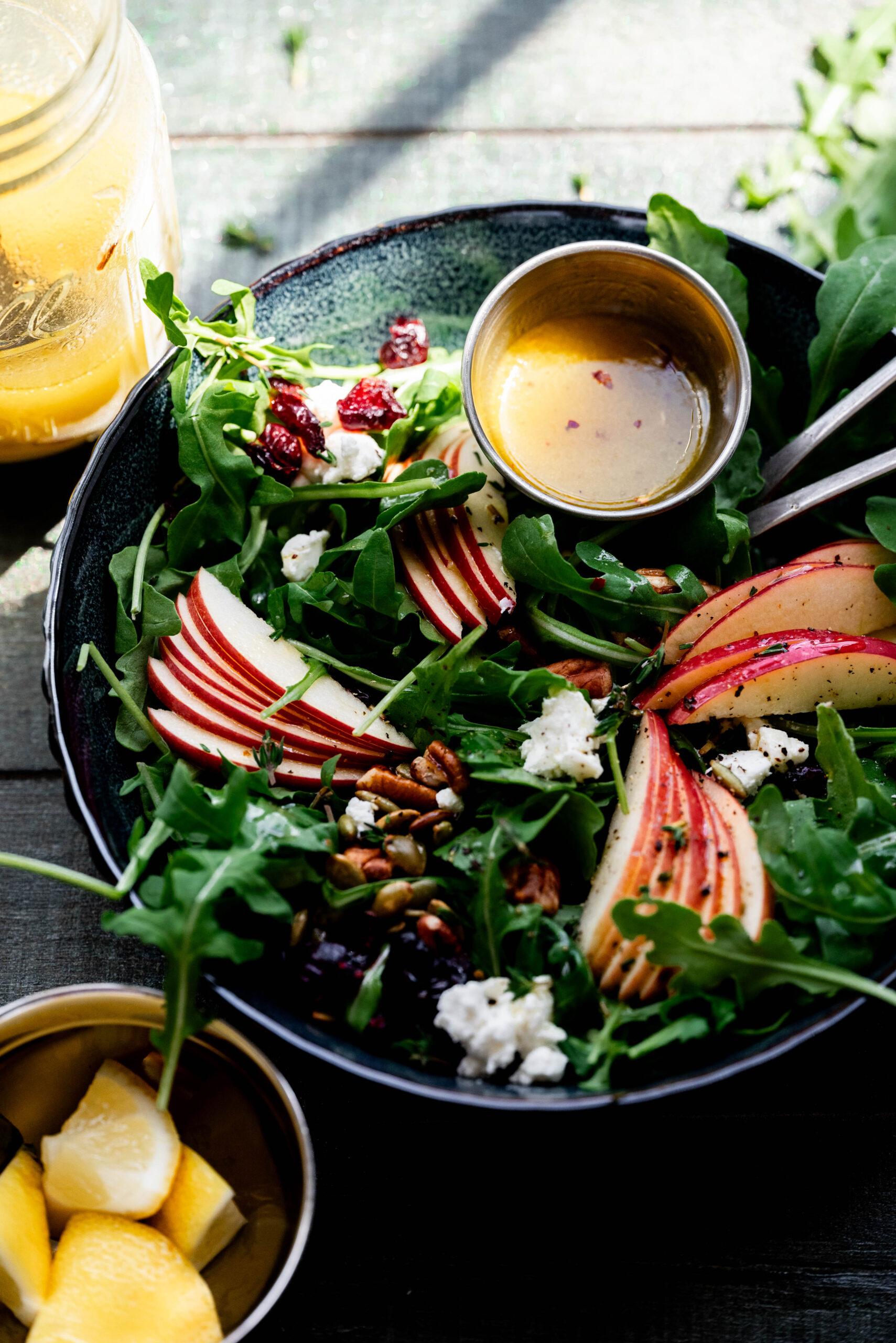 Close-up shot of pear and arugula salad in a black bowl with a side of dressing.