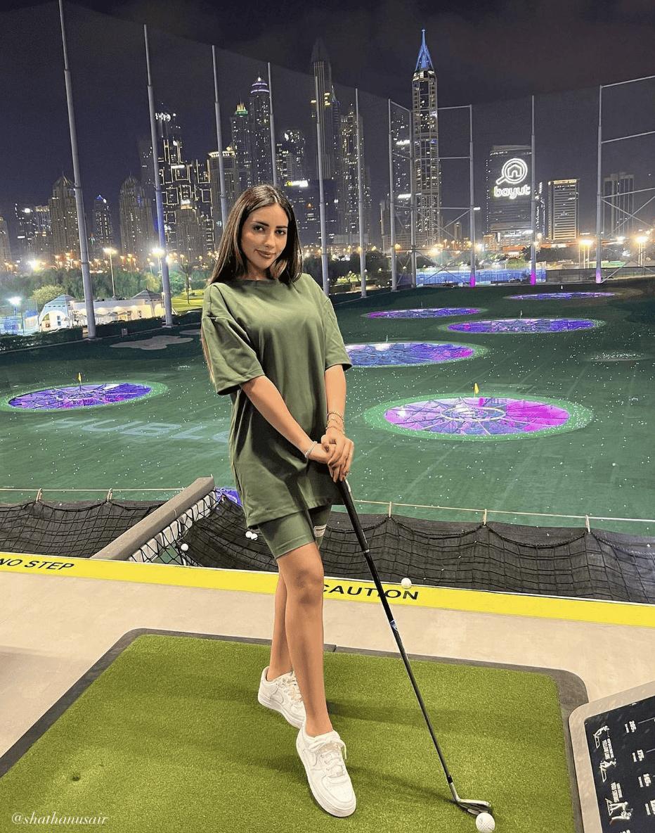 woman at Top Golf wearing a denim jacket over a black crop top with tan cargo pants and black sneakers
