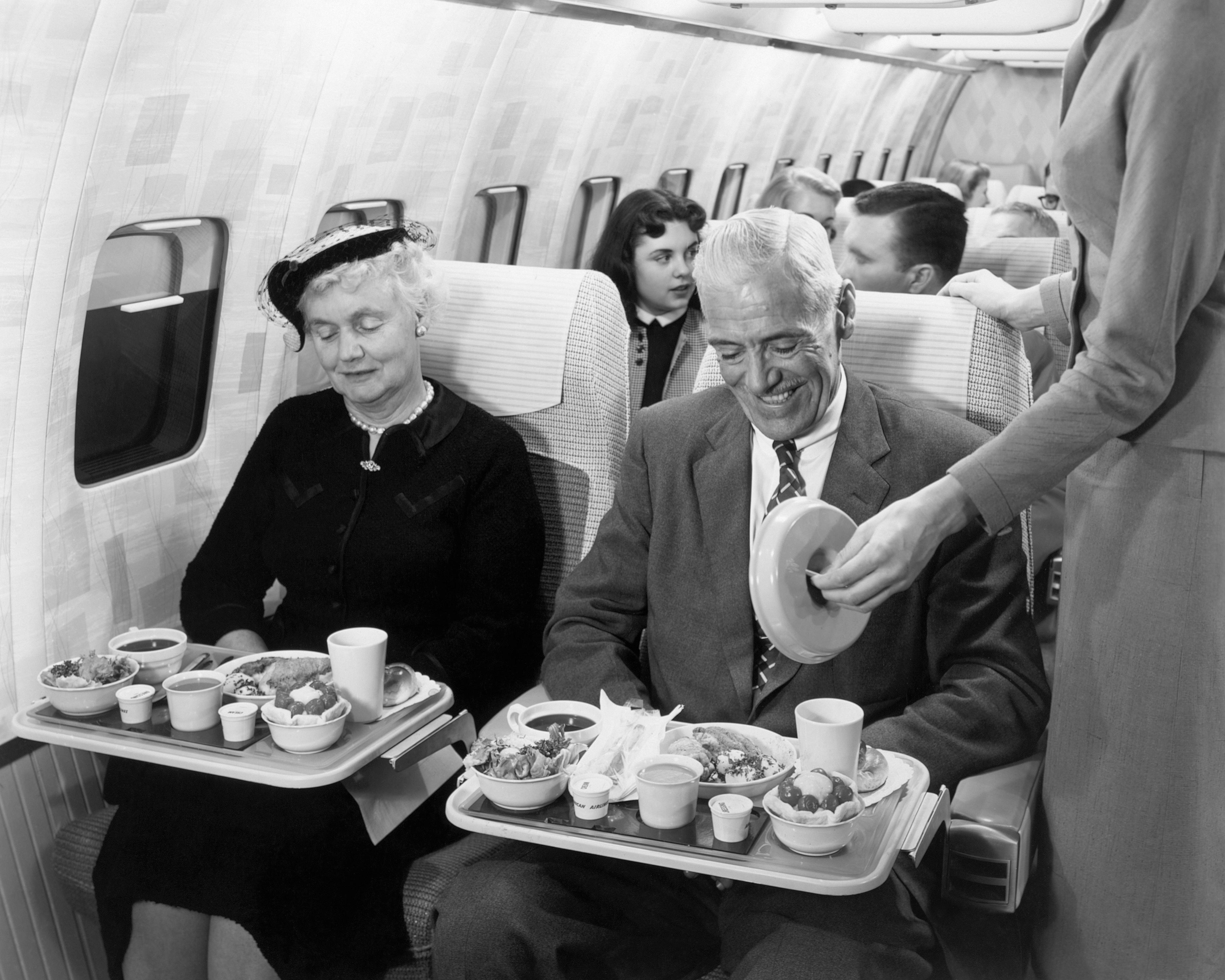 Passengers from the 1950s enjoy a meal inside an airplane.