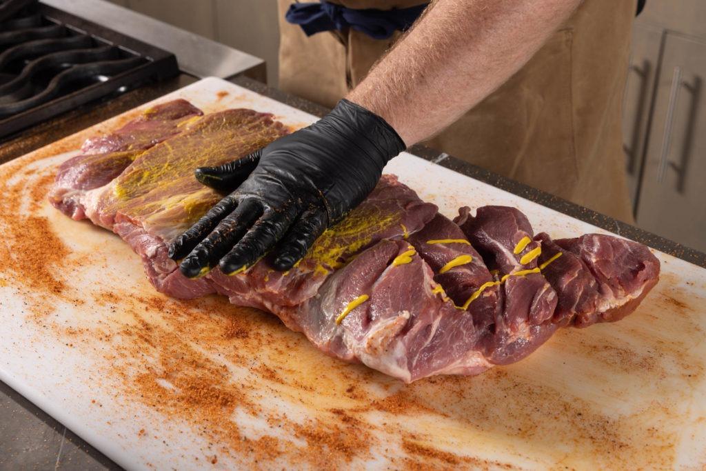 a butterflied pork butt being seasoned