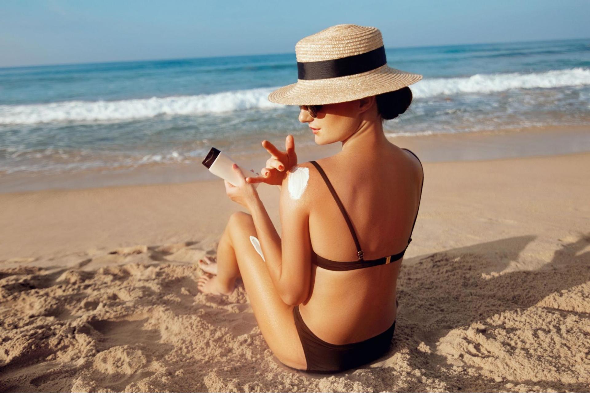 A woman reapplies sunscreen on her shoulder while tanning on the beach