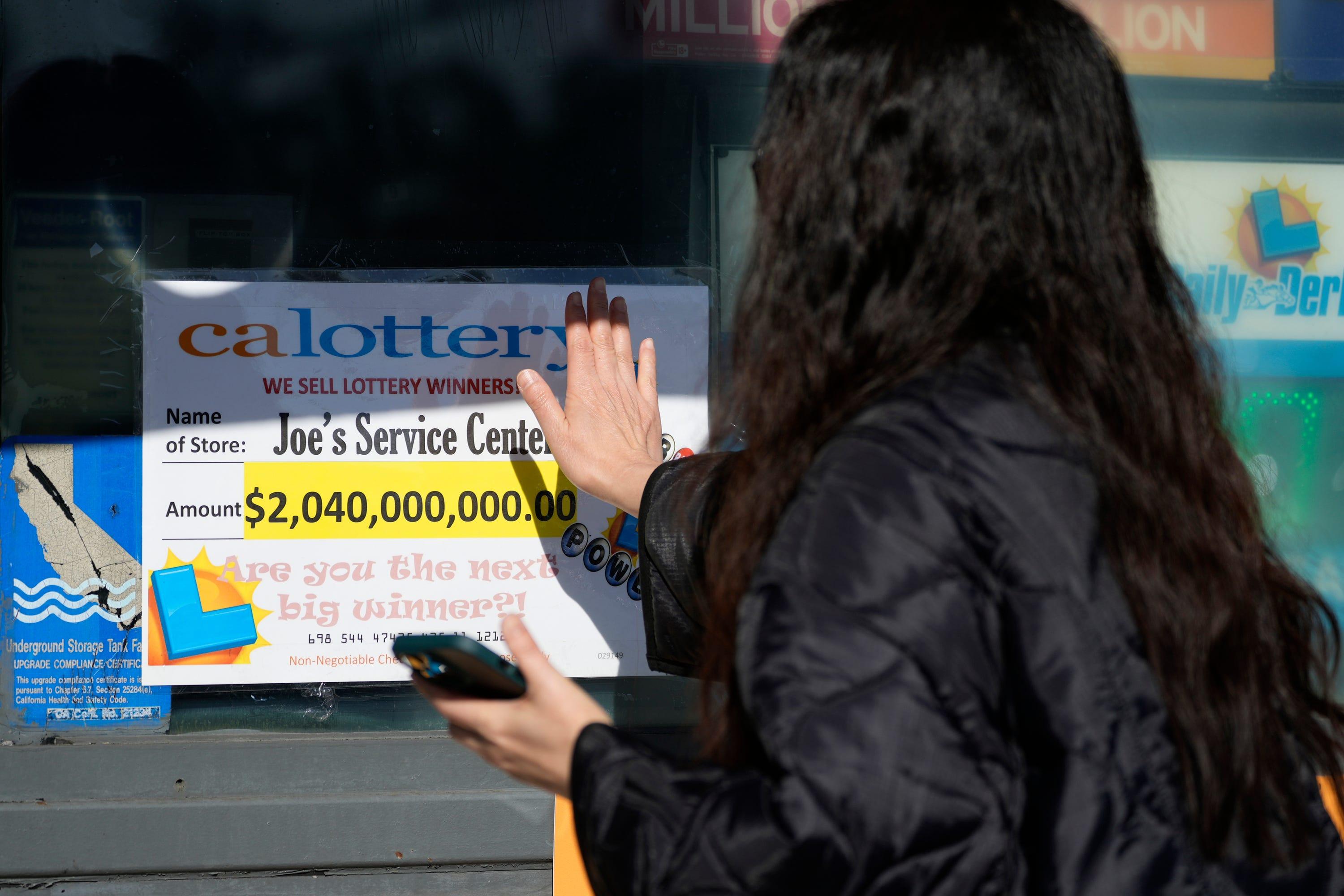 FILE - People touch a window sign for good luck announcing the $2.04 billion-winning Powerball ticket award at Joe