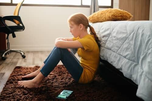 Young girl worried about her acne sitting on rug floor