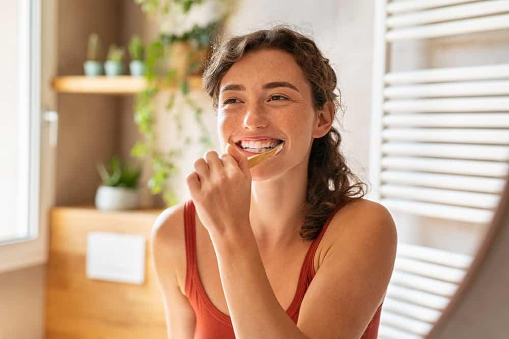 Smiling young woman brushing teeth in bathroom