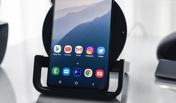 A closeup of a bottom part of an Android phone screen with several app icons. The phone is on a stand