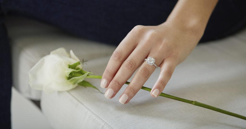 female hand wearing a ring while holding a flower