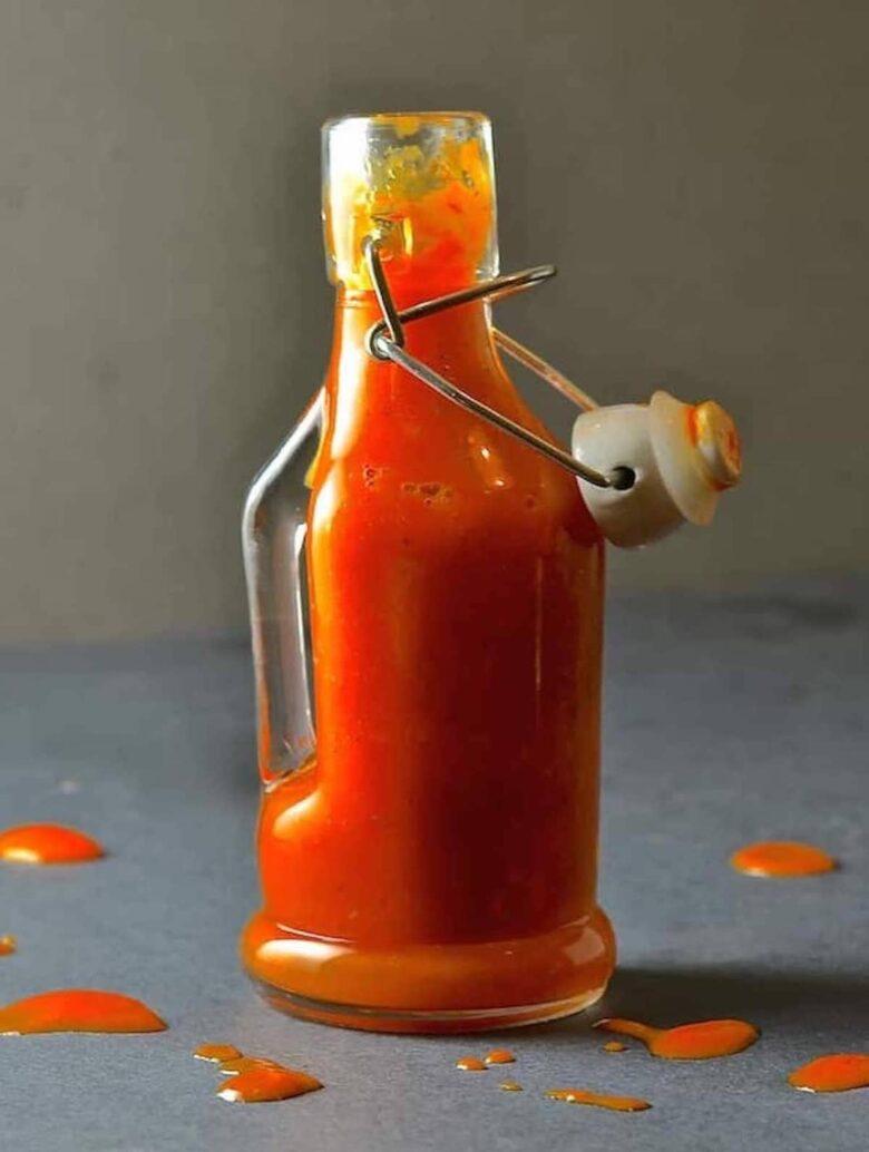 A bottle of hot sauce made from ripe habanero peppers sitting on a table.