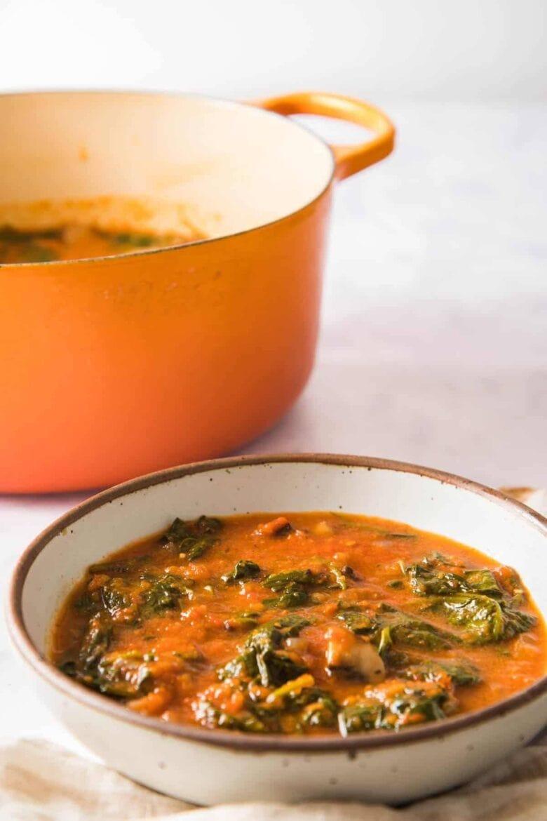 A bowl of Nigerian stew next to an orange pot.