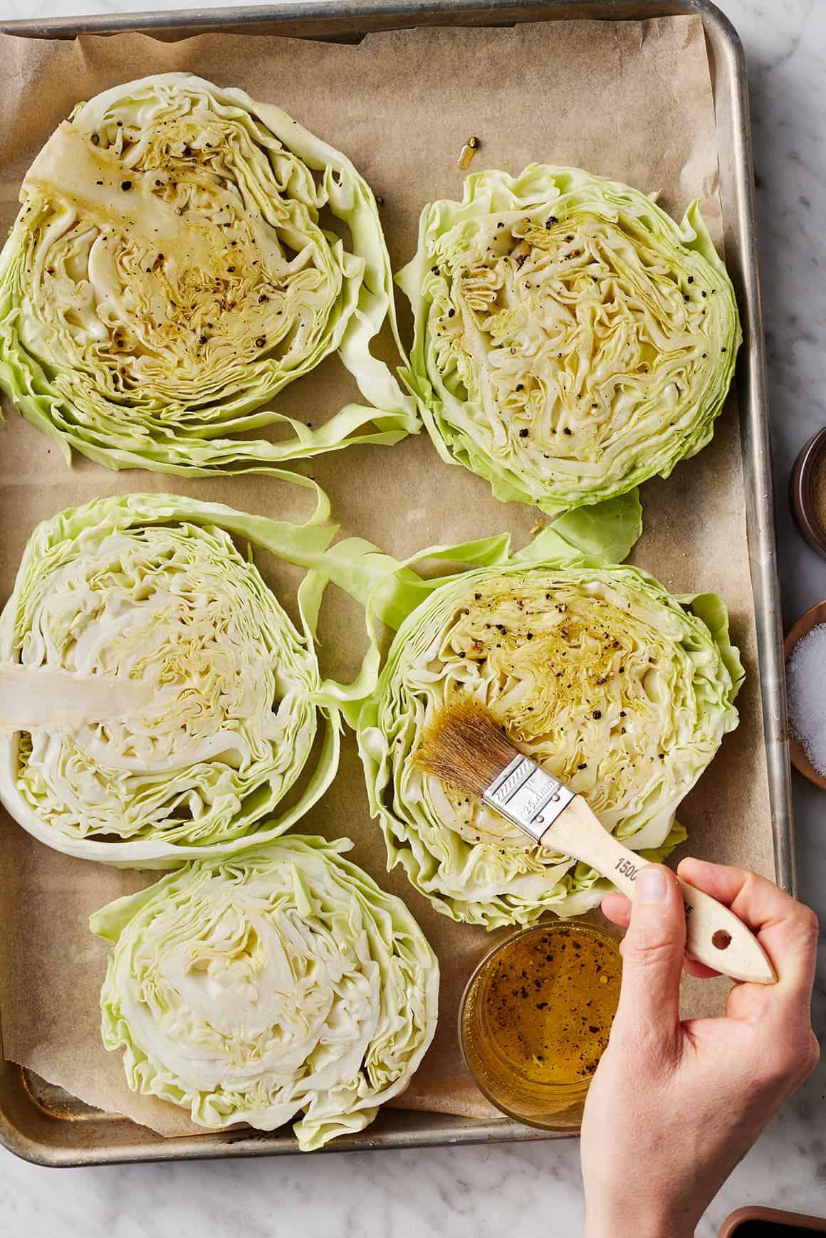 Brushing cabbage steaks with garlic oil on baking sheet lined with parchment paper