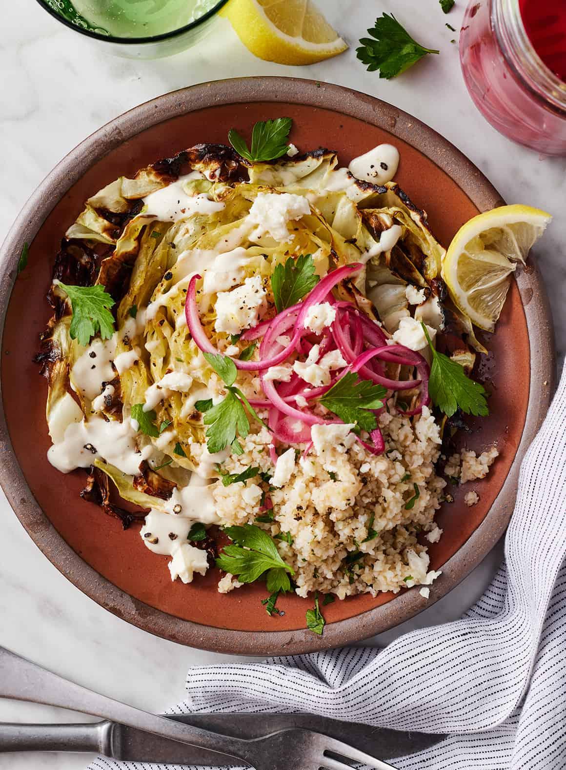 Cabbage steak topped with parsley, tahini sauce, bulgur, and pickled onions