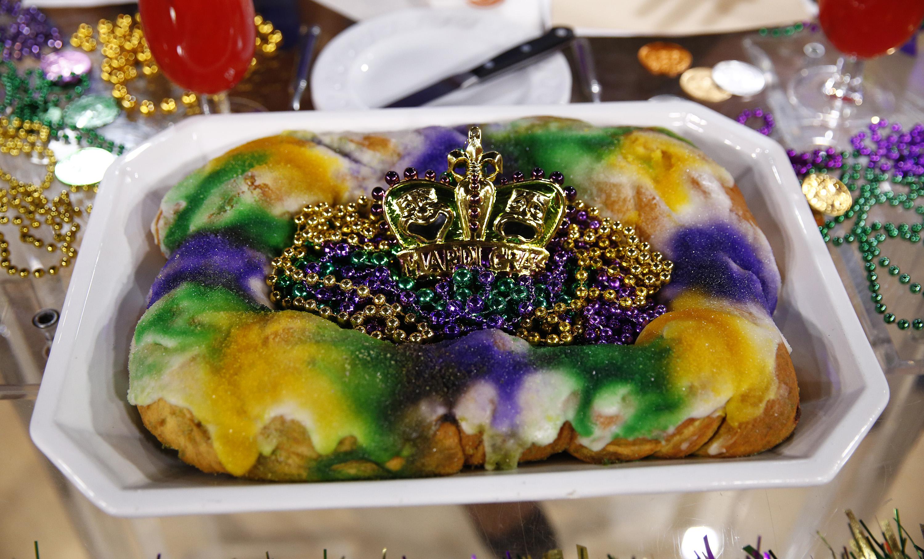 A cake with green, yellow, and purple frosting covered in plastic Mardi Gras beads.